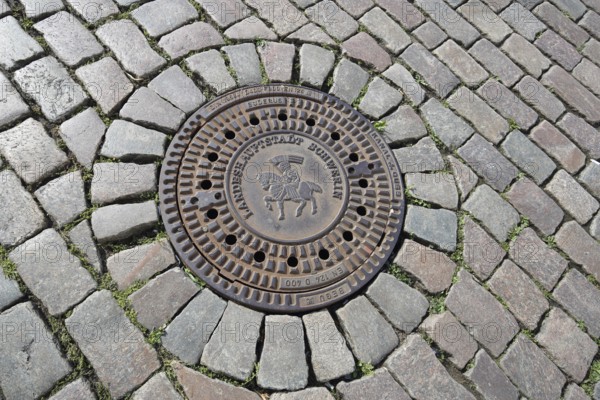 Round manhole cover with city coat of arms and inscription, state capital, paving stones, floor,