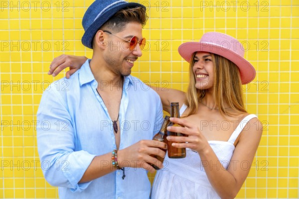 Young stylish tourists toasting with beer bottles, enjoying summer vacation together against a