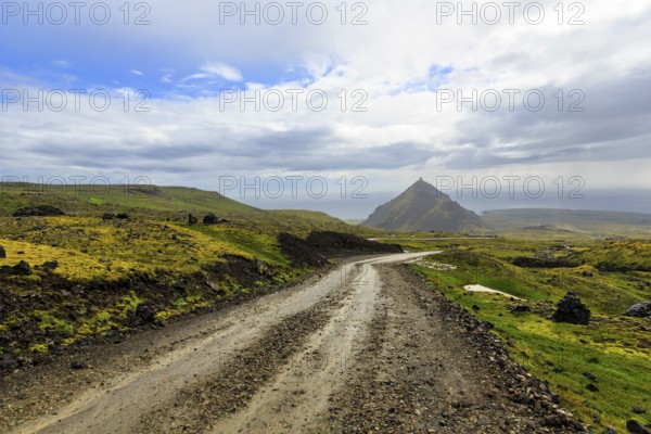 Gravel track through barren moss-covered volcanic landscape, cone-shaped mountain Stapafell, rain