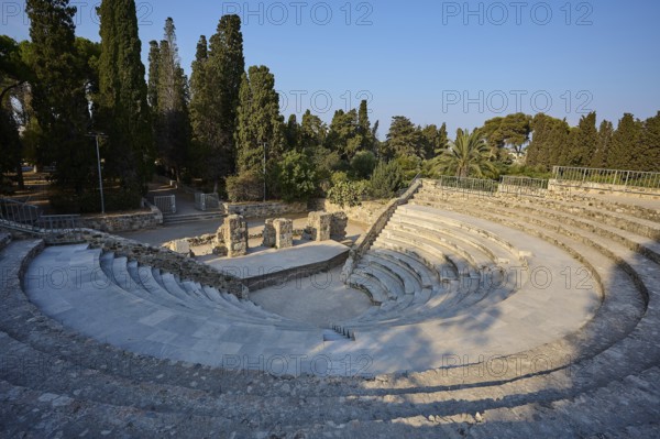 Ancient round amphitheatre with stone steps, surrounded by tall trees and ruins, Ancient Theatre,