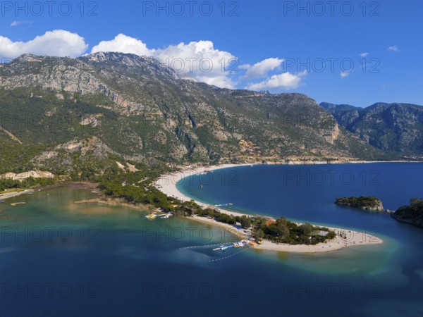 View of a beach with a peninsula surrounded by mountains and blue sea under a clear sky with