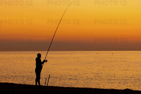 A man fishing just in front of sunrise on the Costa Rei, a coastline of the Italian island of