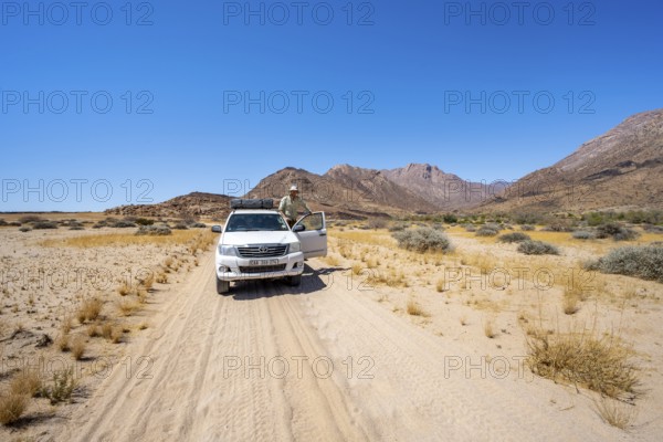 Young man standing in the open door of an off-road vehicle, sandy track, desert landscape with