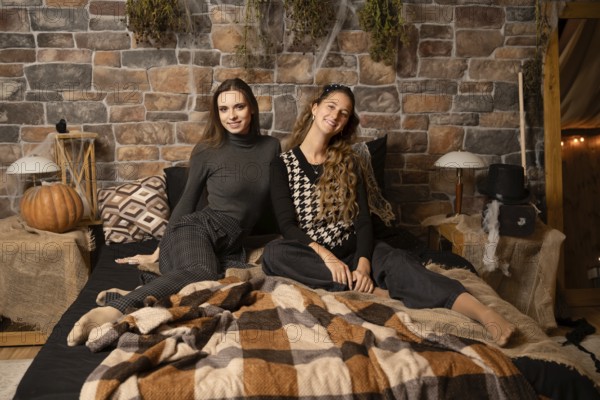 Two women enjoy a relaxed moment together on a warm blanket in a rustic bedroom filled with autumn