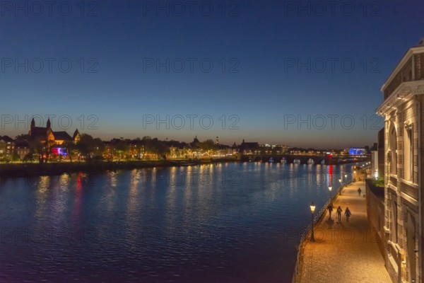 Maastricht, Netherlands, night view of the river Maas with illuminated bridge and promenade, under