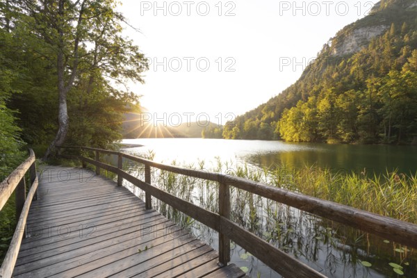 Sunrise in summer at Lake Thumsee near Bad Reichenhall with a wooden footbridge and a sun star over
