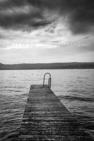 A rustic jetty stretches into the calm waters of Lake Geneva, framed by gentle waves and majestic