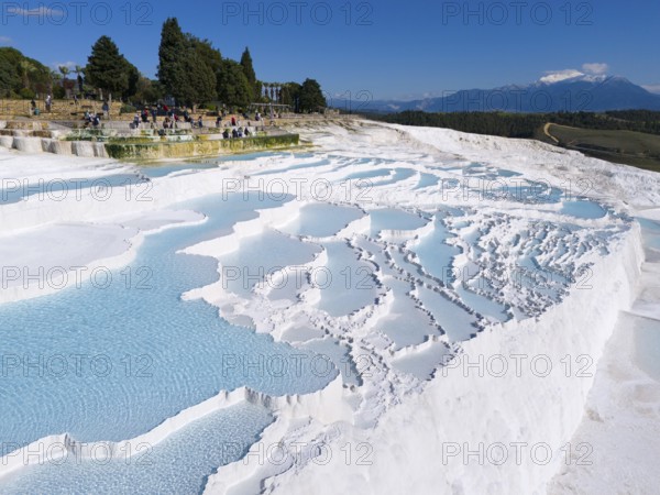 View of limestone terraces with turquoise blue water surrounded by trees and tourists, aerial view,