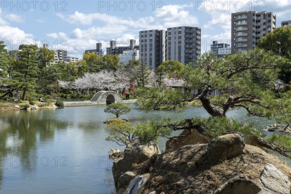 Shukkei-en with Sekisui-gan stone formation, green plants, trees and Koko-kyo stone bridge over