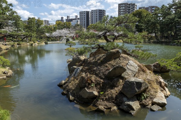 Shukkei-en with Sekisui-gan stone formation, green plants, trees and Koko-kyo stone bridge over