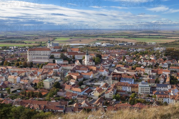 Panoramic view of a town with a historic castle and churches, surrounded by fields and clouds,