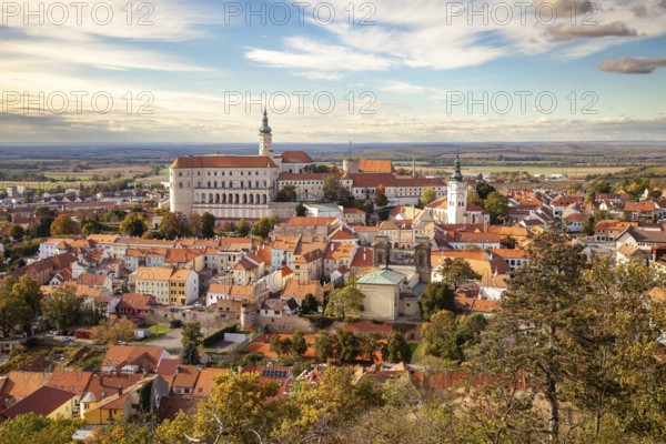 Panorama of a historic town with castle and churches, surrounded by autumn trees and a wide sky,