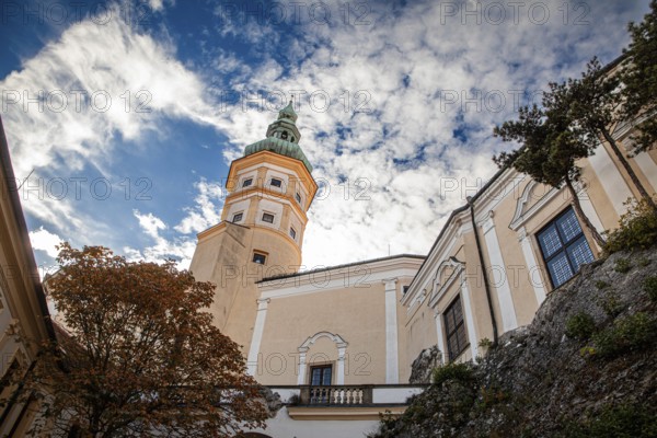 A striking tower stands out against a cloudy sky, next to it an autumn-coloured tree, Mikulov