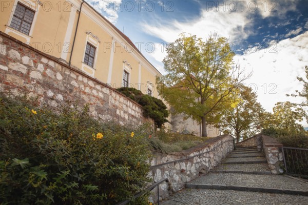 An idyllic path with stone steps and autumn trees leads to a yellow building, Mikulov Nikolsburg