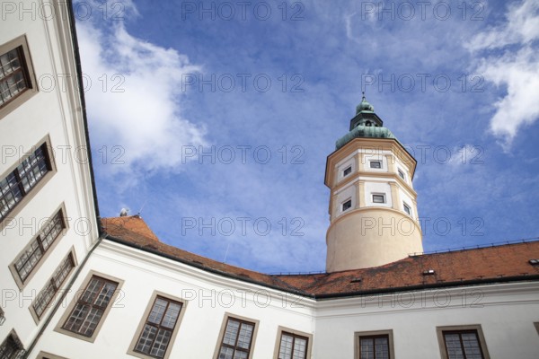 A historic tower rises under a clear blue sky, surrounded by buildings with red tiled roofs,