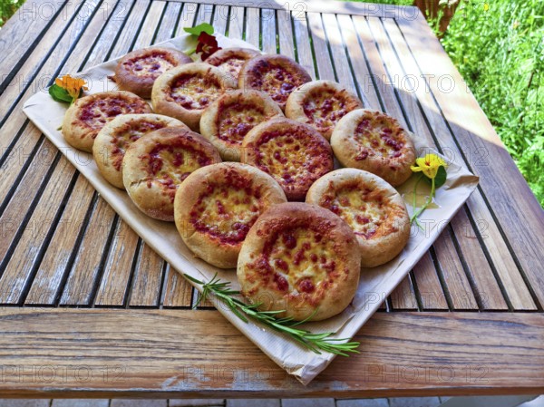 Several small pizzas on a wooden board decorated with flowers, presented on a garden table, Lower