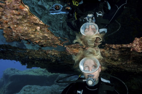Diver with open blonde hair reflected in large air bubble in cave ceiling in underwater grotto,
