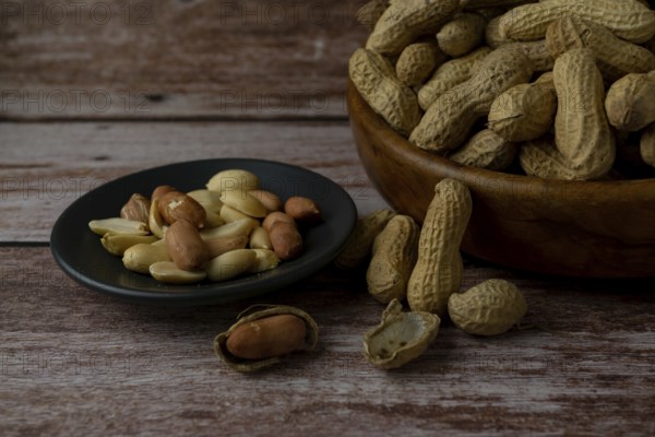 Peanuts in a wooden bowl and peeled peanuts on a plate with a spoonful of peanut butter