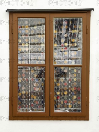 Window with decorative coin collection behind glass, framed by a simple wooden structure Mödling