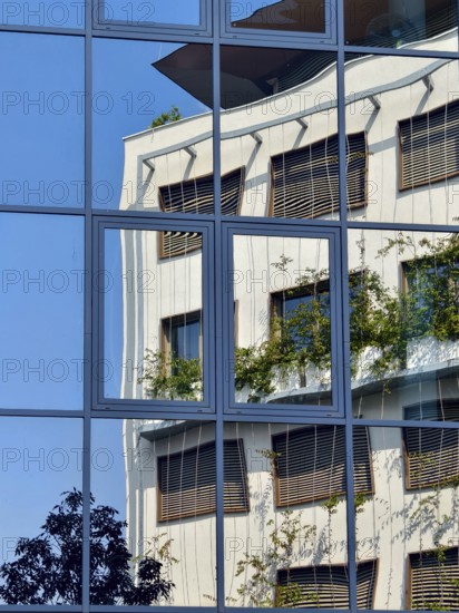 Reflection of a modern building with glass façade and greenery under a blue sky Mödling Lower