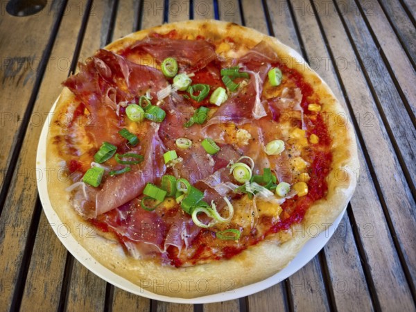 Pizza with ham and spring onions served on a table. Hearty and fresh with an Italian flavour