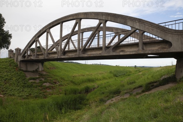 A concrete arch of the bridge stretches across a green meadow under a clear sky Perschling Flood
