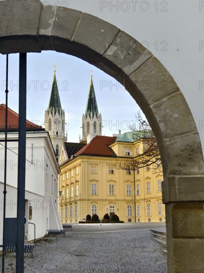 View through a stone gate onto a baroque building with two Gothic church towers, Klosterneuburg