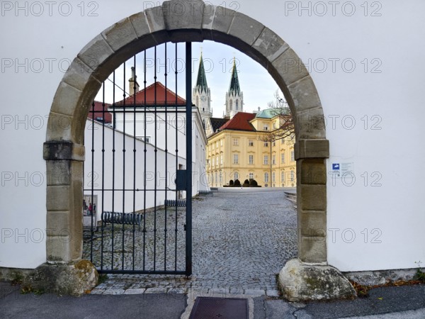 View through a Tor tor to a cobbled courtyard and church towers of a historic building,