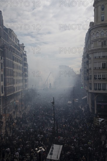 A large crowd gathers in a smoky city street MascletÃ¡ de Fallas