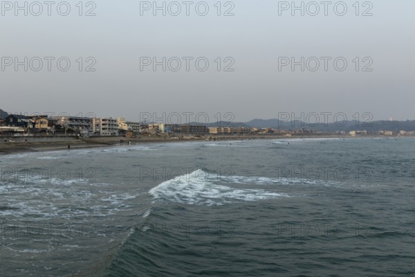 Houses on the seafront and surfers in the surf at dusk on the beach in Kamakura, Kanagawa