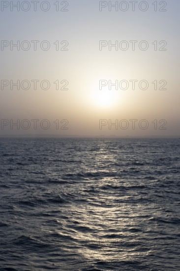Background image, setting sun with silhouette of land, water surface in evening light, waves in the