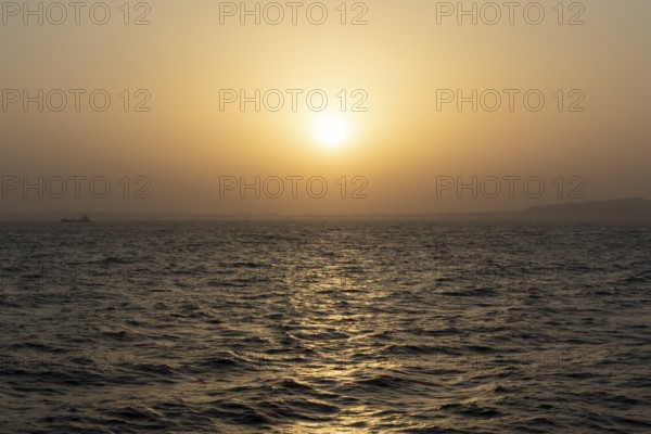 Background image, setting sun with silhouette of land, water surface in evening light, waves in the