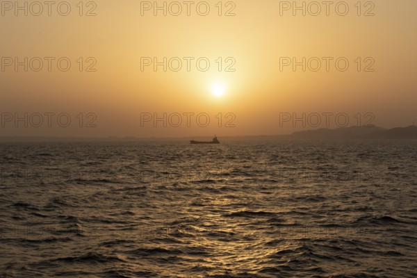 Background image, setting sun with silhouette of ship and land, water surface in evening light,