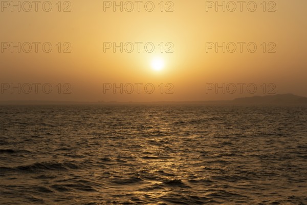 Background image, setting sun with silhouette of land, water surface in evening light, waves in the