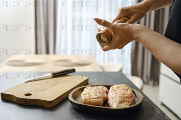 A person seasons fresh duck fillets with sea salt in a stylish kitchen. The wooden cutting board