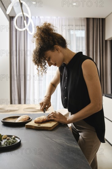 A woman is focused on cutting duck fat in a kitchen. Natural light fills the space, enhancing the