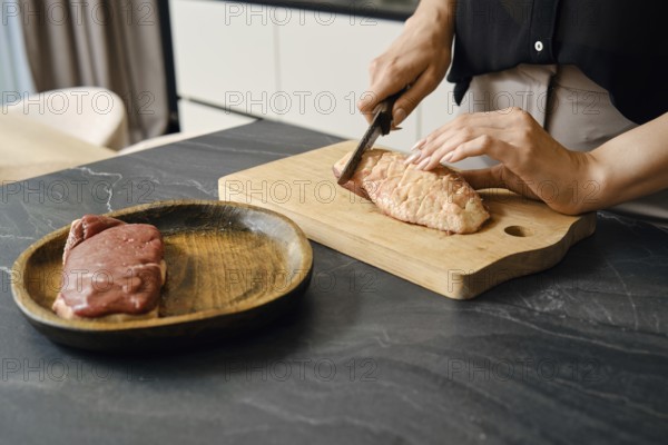 A person skillfully cuts the skin crosswise on a duck breast on a wooden board placed on a dark
