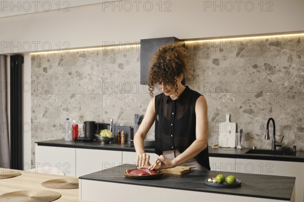 A woman takes duck meat from a wooden plate in a sleek modern kitchen. The kitchen features