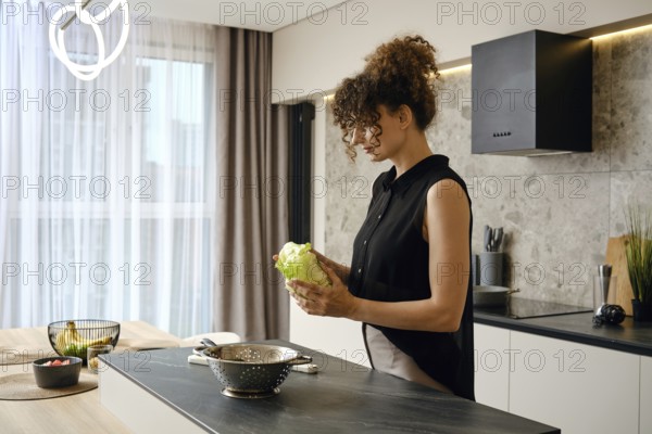 In a contemporary kitchen filled with natural light, a woman holds a head of lettuce while