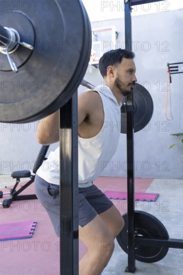 Focused male athlete is strengthening his legs by performing squats with a weighted barbell in a