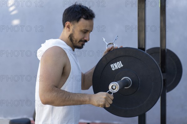 Focused male athlete meticulously secures weight plates onto a barbell, preparing for an intense