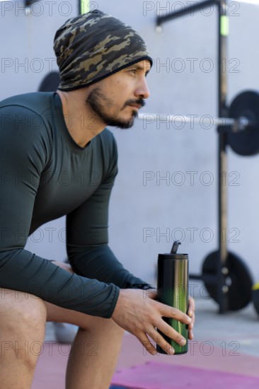 Athlete sitting and taking a break after an intense workout, holding a water bottle and emphasizing