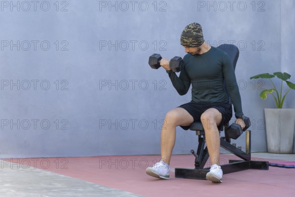 Focused athlete performs bicep curls with dumbbells, seated on a weight bench, showcasing
