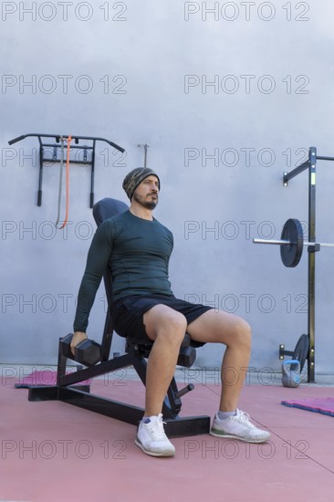 Athlete is strengthening his deltoids by performing seated lateral raises with dumbbells in an