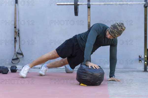 Focused male athlete wearing a beanie performing one-handed push-ups on a medicine ball in an