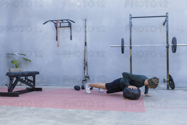 Young athlete performing push-ups with hands on a medicine ball in an outdoor gym, showcasing