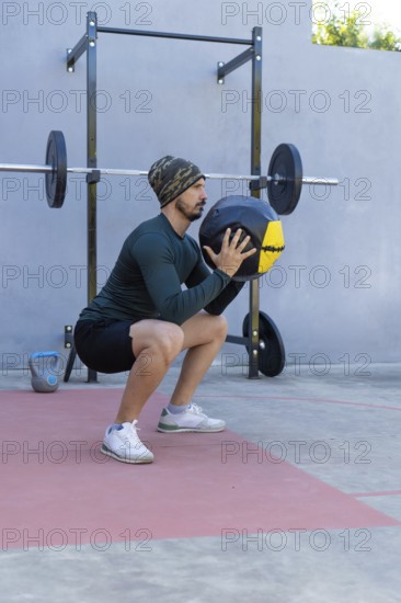 Young sportsman performing squats with a medicine ball in an outdoor gym, demonstrating strength