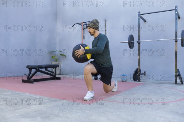 Athlete performing lunges while gripping a medicine ball in an outdoor gym, demonstrating strength