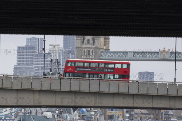 Red double decker bus driving over a bridge with Tower bridge in the background, City of London,