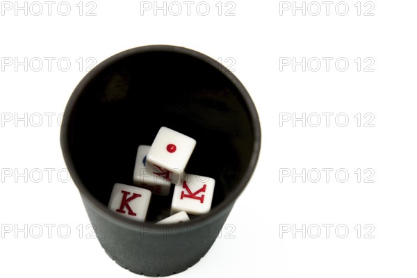 Four white dice showing king and one resting in a black dice cup on a white background, suggesting